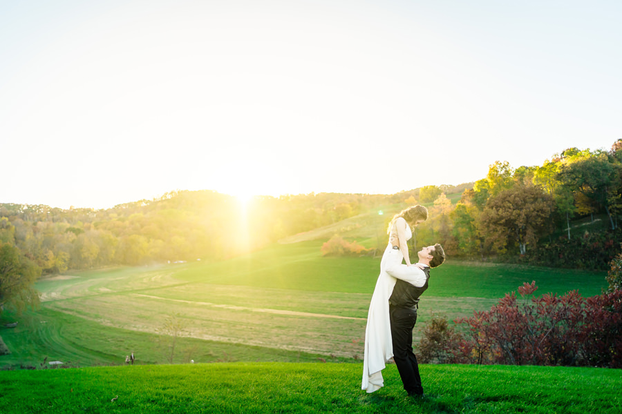 A bride and groom standing on a grassy field at sunset.