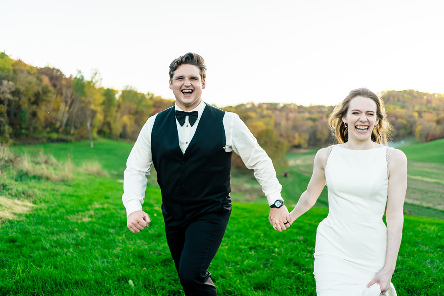 A bride and groom running together in a field.