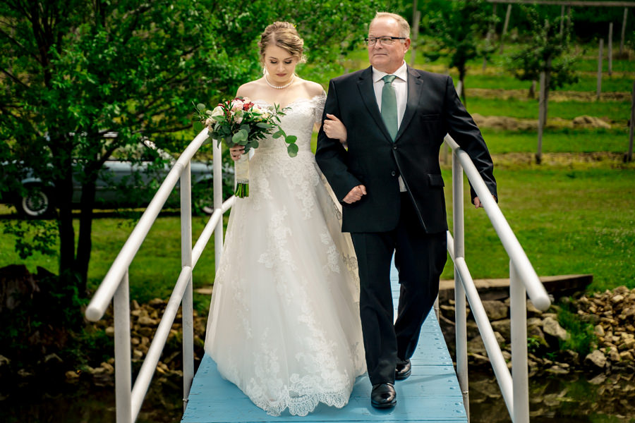 A bride and her father walking across a bridge.