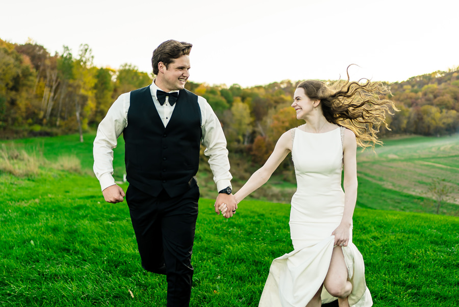 A bride and groom running in a field.