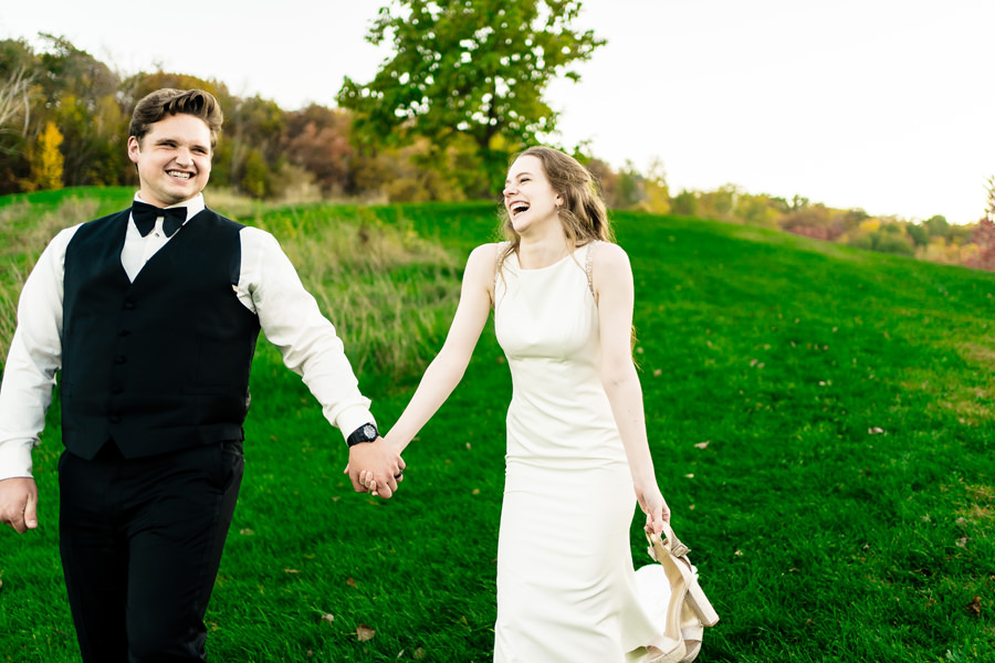 A bride and groom holding hands in a grassy field.