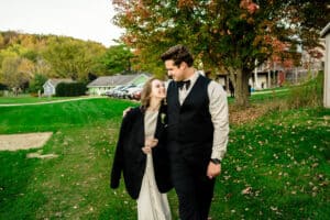 A bride and groom walking through a grassy field.