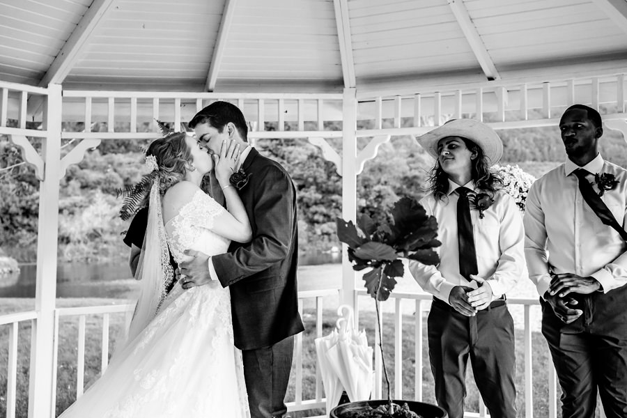 A bride and groom kiss in front of a gazebo.