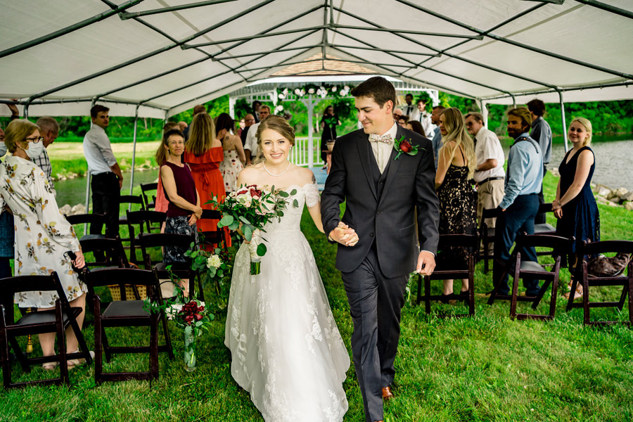 A bride and groom walking down the aisle in a tent.