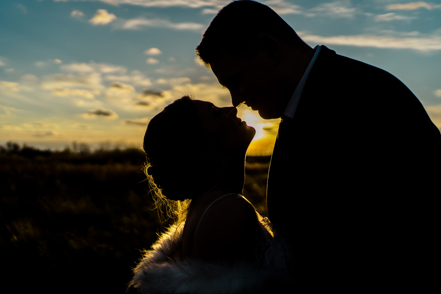 A silhouette of a bride and groom kissing at sunset.