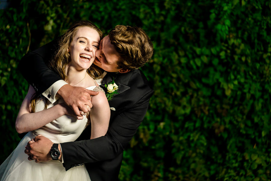 A bride and groom hugging in front of a green wall.