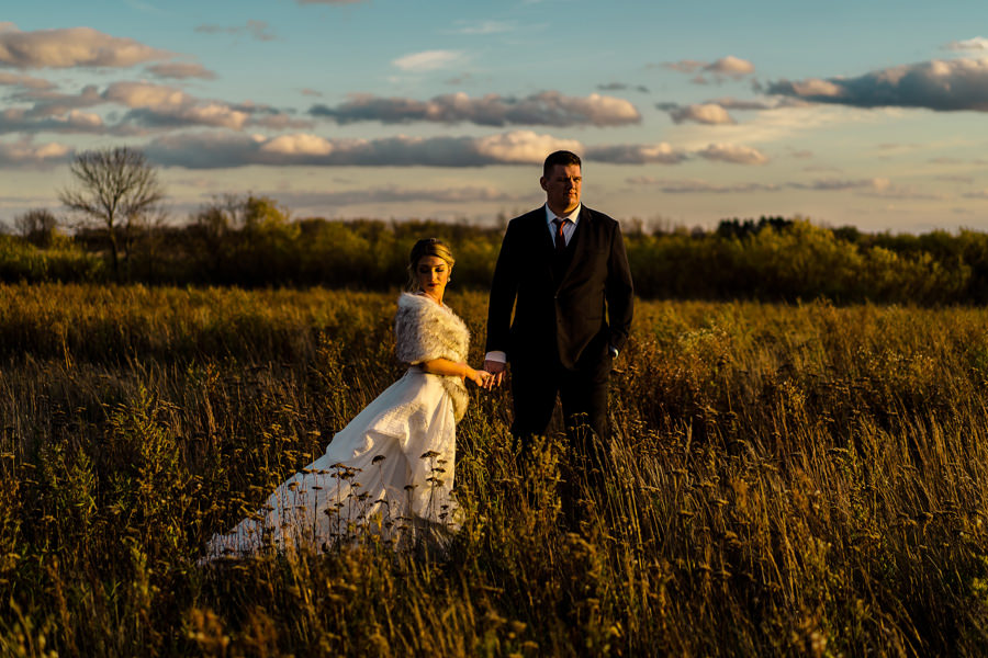 A bride and groom standing in a field at sunset.