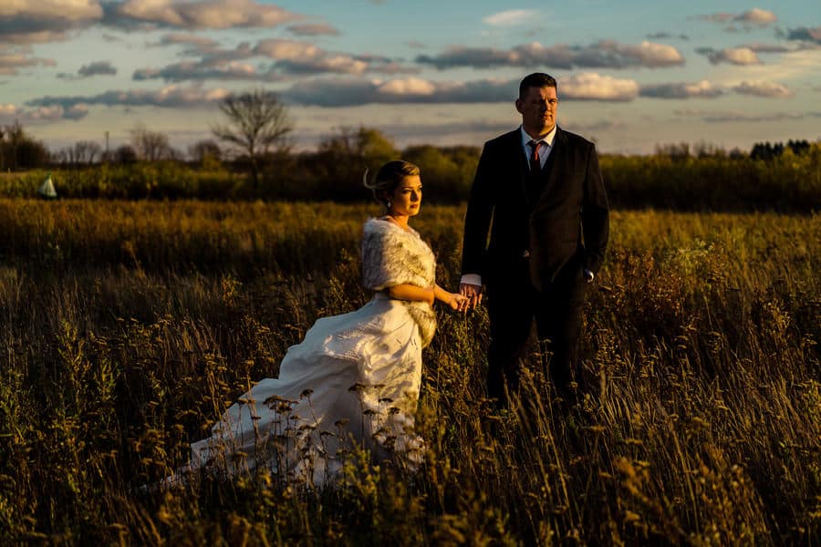 A bride and groom standing in a field at sunset.