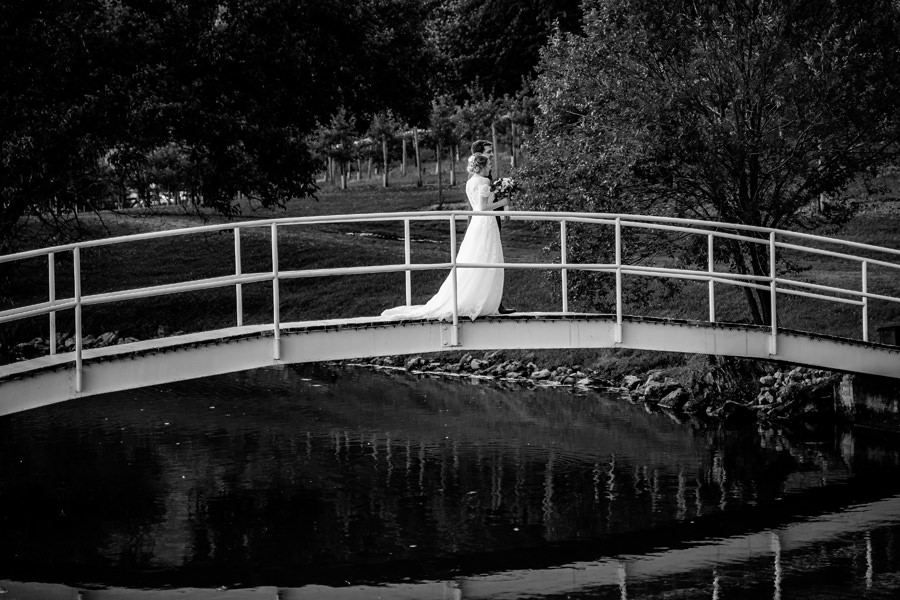 A bride standing on a bridge over a pond.