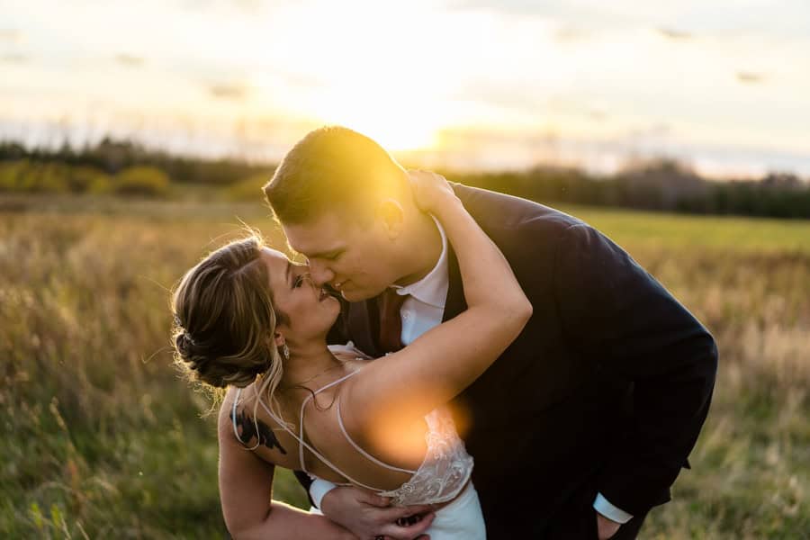 A bride and groom kissing in a field at sunset.