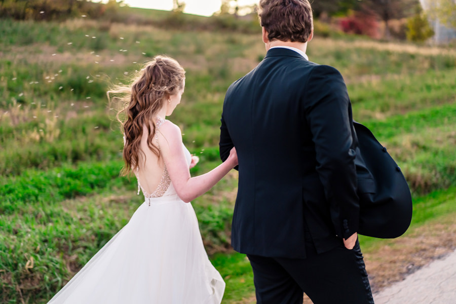 A bride and groom walking down a path in a field.
