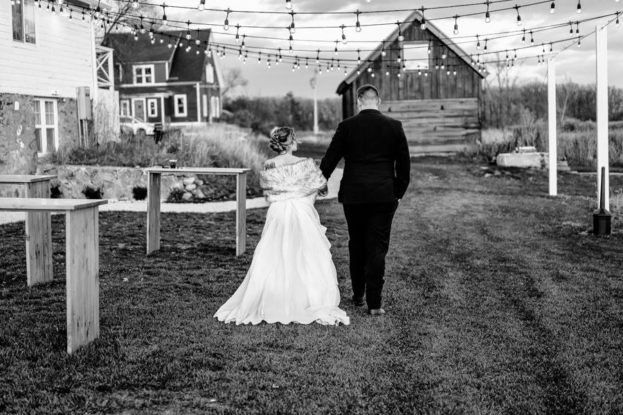 A bride and groom walking down a path with string lights.