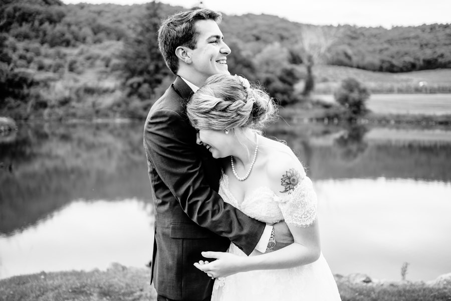 A bride and groom hugging in front of a pond.