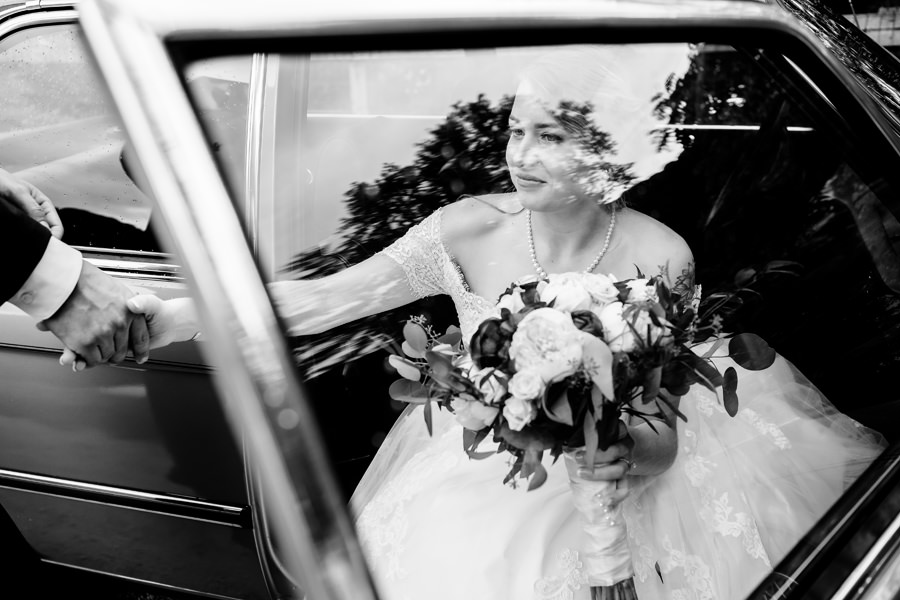 A black and white photo of a bride and groom getting out of a car.