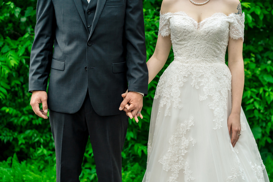 A bride and groom holding hands in front of bushes.