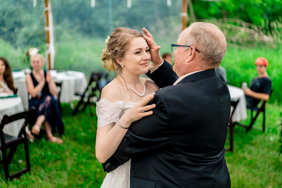 A bride dances with her father in a grassy field.