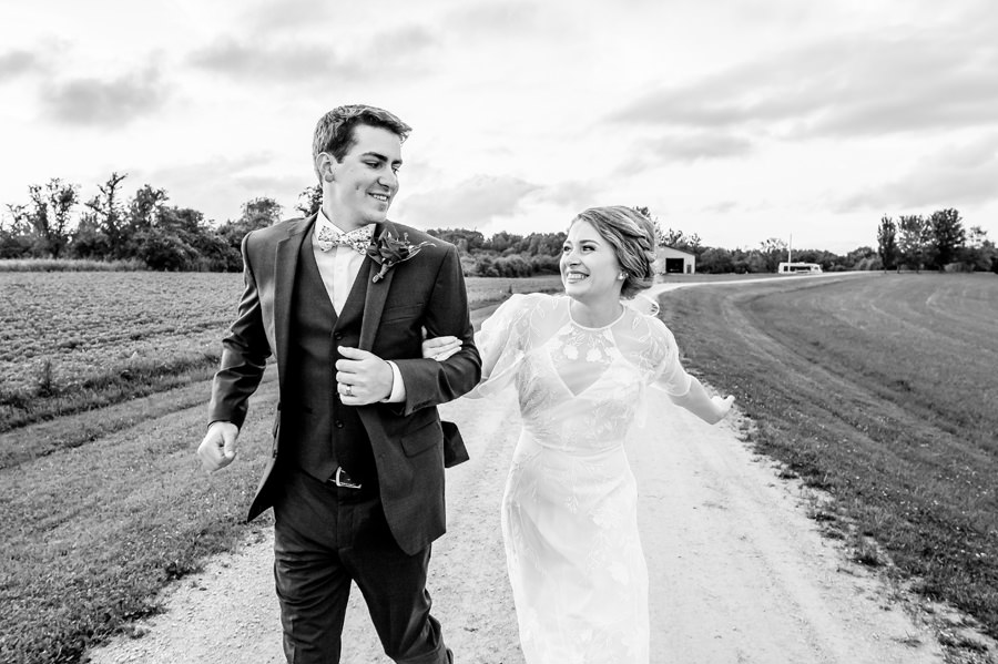 A bride and groom running down a dirt road.