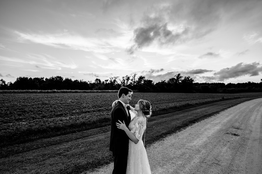 A bride and groom standing on a dirt road.