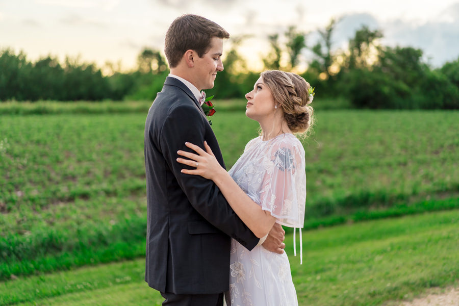 A bride and groom embrace in the middle of a field.