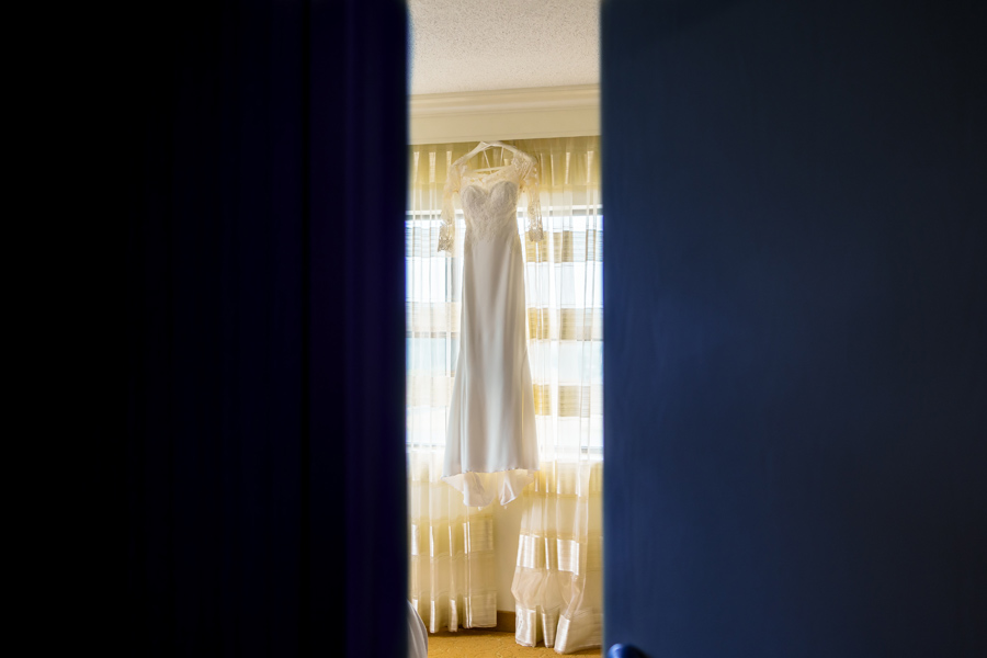 A wedding dress hangs on a hanger in a room.