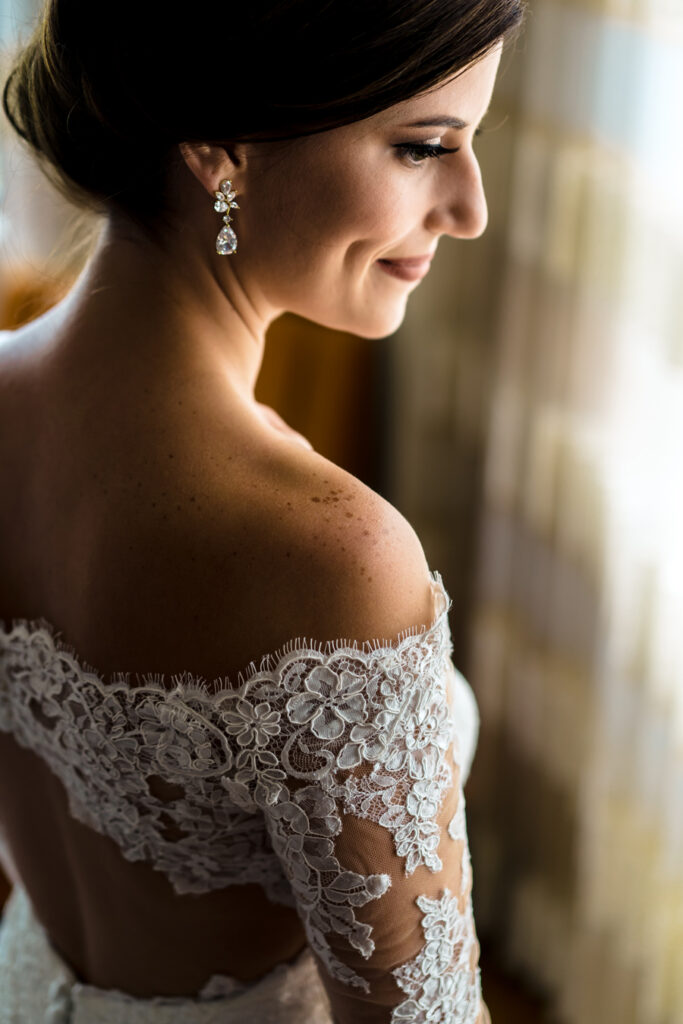 A bride in an off the shoulder wedding dress looking out the window.