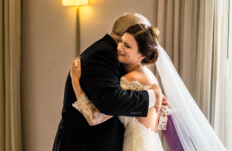 A bride hugging her father in a hotel room.