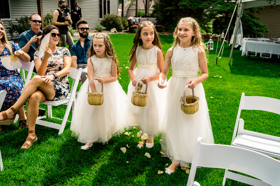 Three little girls in white dresses walking down the aisle.