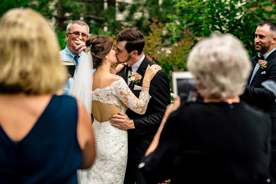 A bride and groom kiss during their outdoor wedding ceremony.