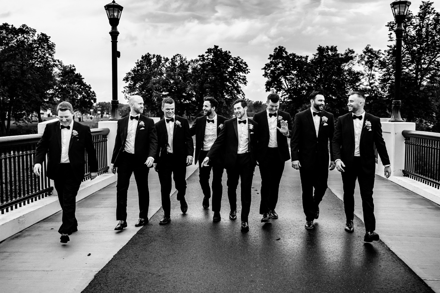 A black and white photo of a group of groomsmen walking on a bridge.