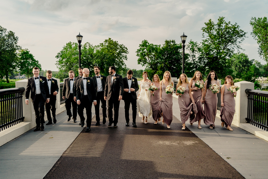 A group of bridesmaids and groomsmen walking on a bridge.