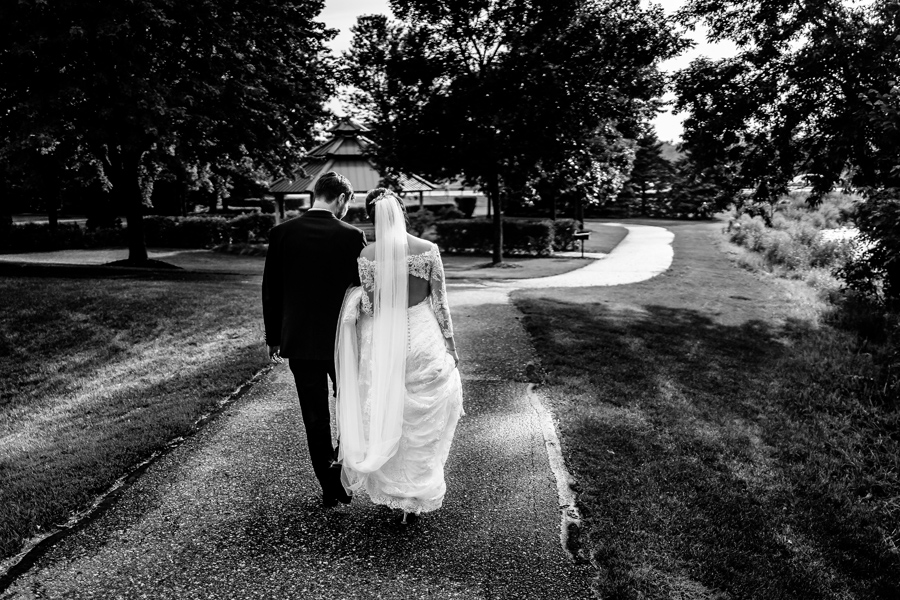 A bride and groom walking down a path in black and white.