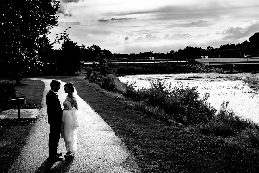 A bride and groom standing next to a river in black and white.