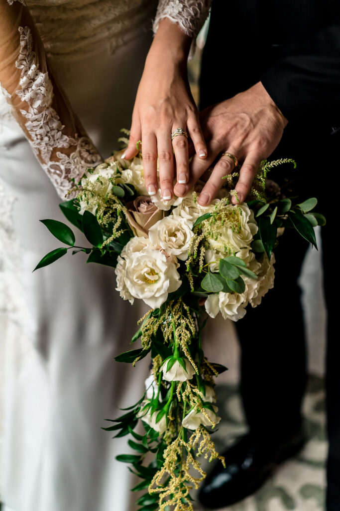 A bride and groom's hands holding a bouquet of flowers.
