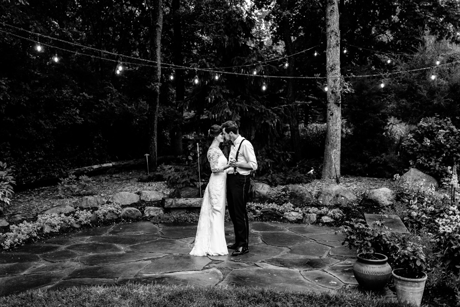 A black and white photo of a bride and groom kissing in the woods.