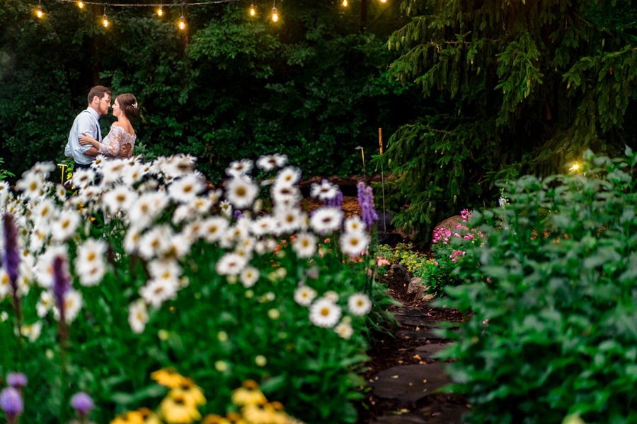 A couple kisses in a garden under string lights.