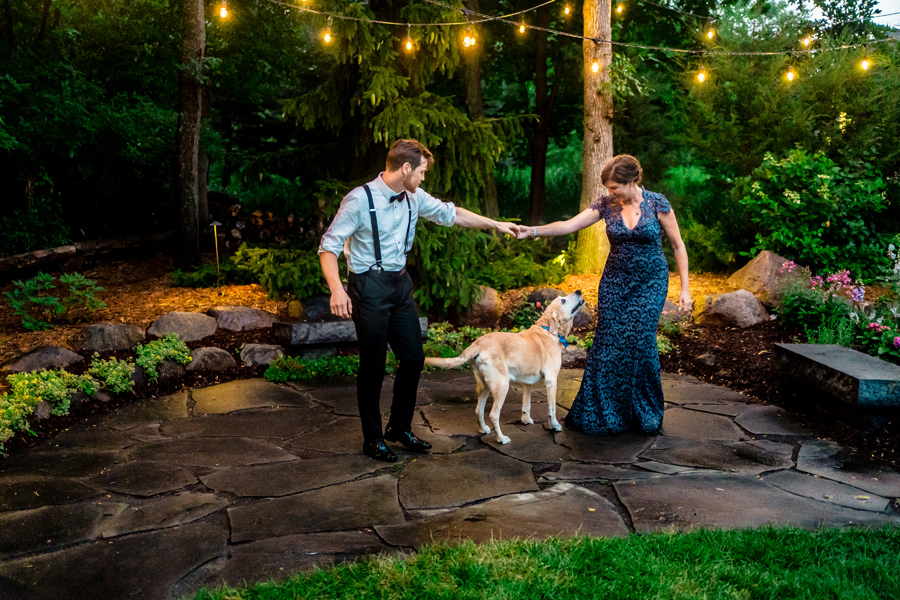 A bride and groom with their dog in a garden.