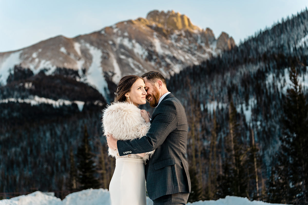 A bride and groom embrace in front of the mountains during their winter elopement.
