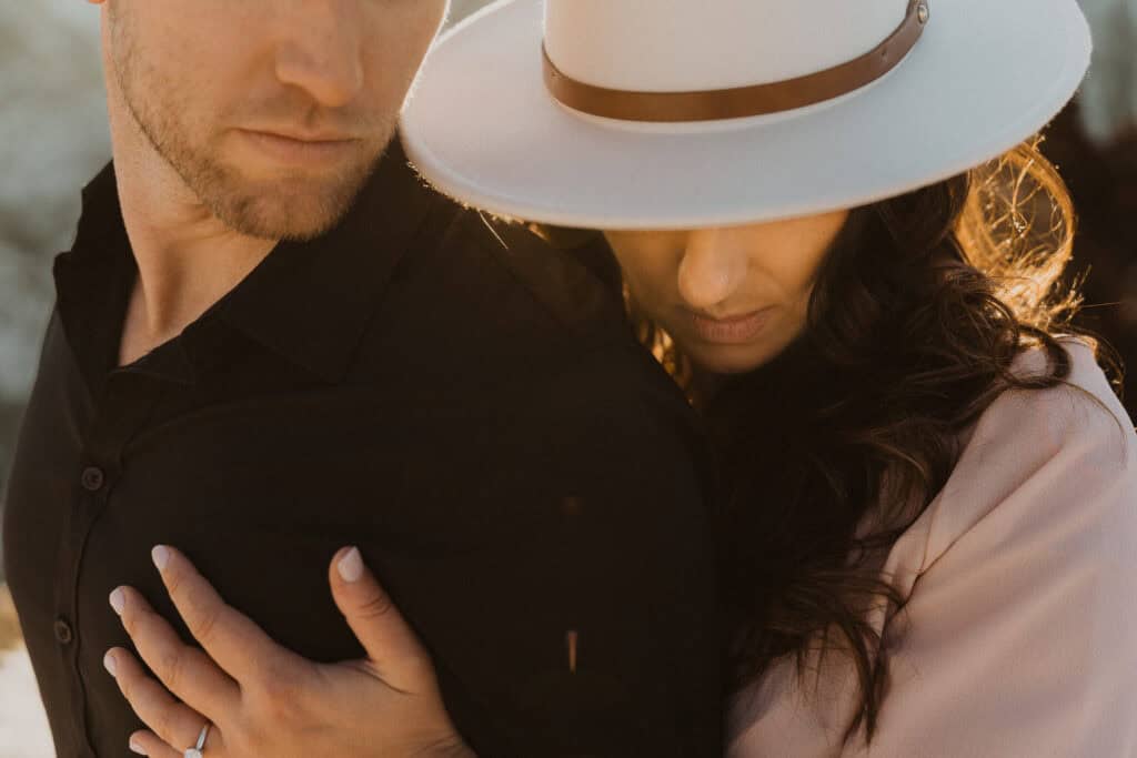A man and woman in a white hat are embracing in the snow, capturing the essence of an ultimate winter wedding.