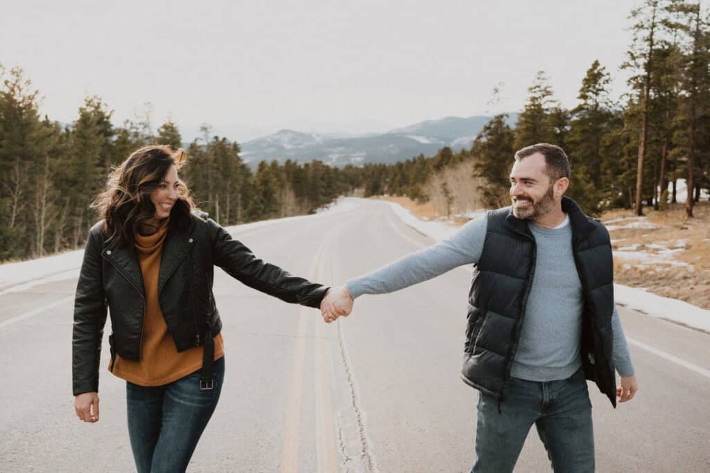 A couple holding hands on a road in the mountains.