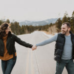 A couple holding hands on a road in the mountains.