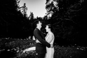 A bride and groom embracing by a river in black and white.