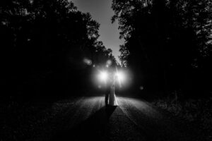 A black and white photo of a woman walking down a dark road.