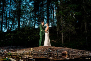 A bride and groom standing on a rock in the woods.