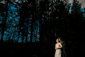 A bride and groom standing in front of a tree in the woods.