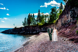 A bride and groom walking on a rocky path near the water.