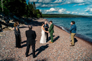 A bride and groom standing on the shore of a lake.