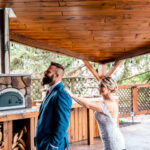 A emotional backyard wedding with a bride and groom standing next to an outdoor pizza oven in La Crosse.