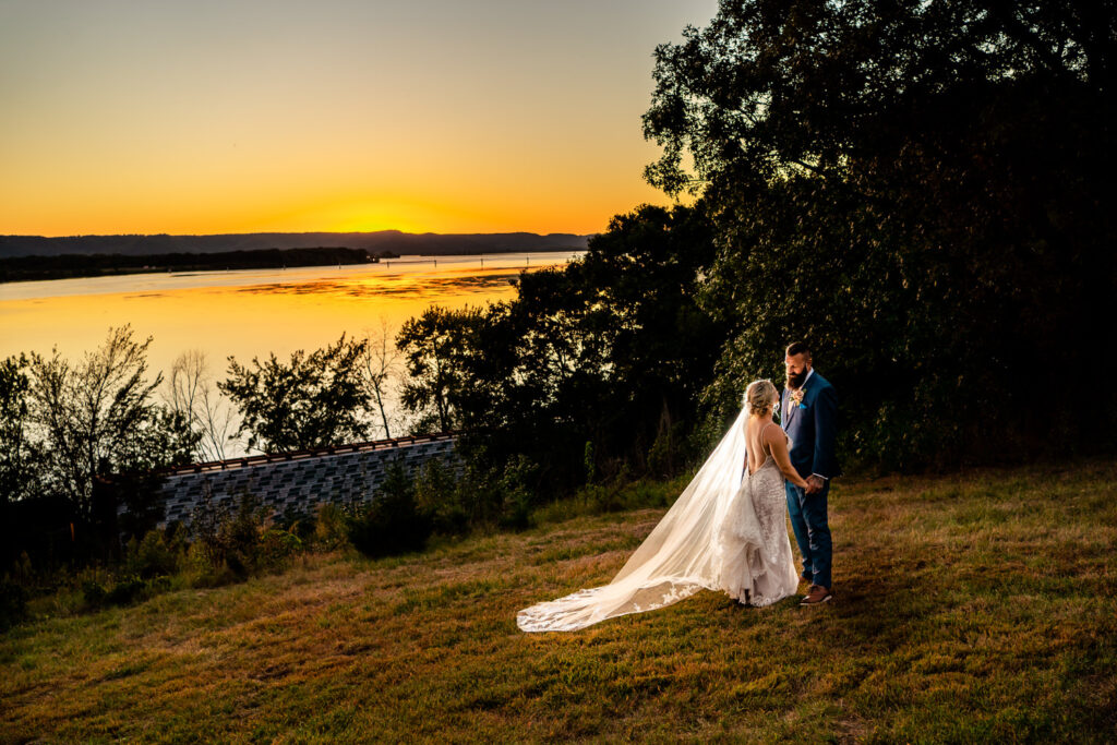 An emotional backyard wedding with the bride and groom standing on a hill overlooking a lake at sunset in La Crosse.