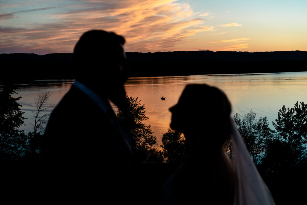 A backyard wedding in La Crosse featuring a silhouetted bride and groom, standing in front of a lake at sunset, evoking emotional moments.