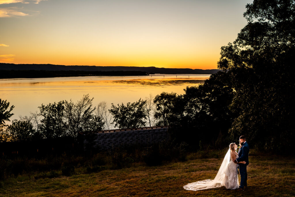 A couple emotionally exchanging vows at a La Crosse backyard wedding, standing on a hill overlooking a river at sunset.